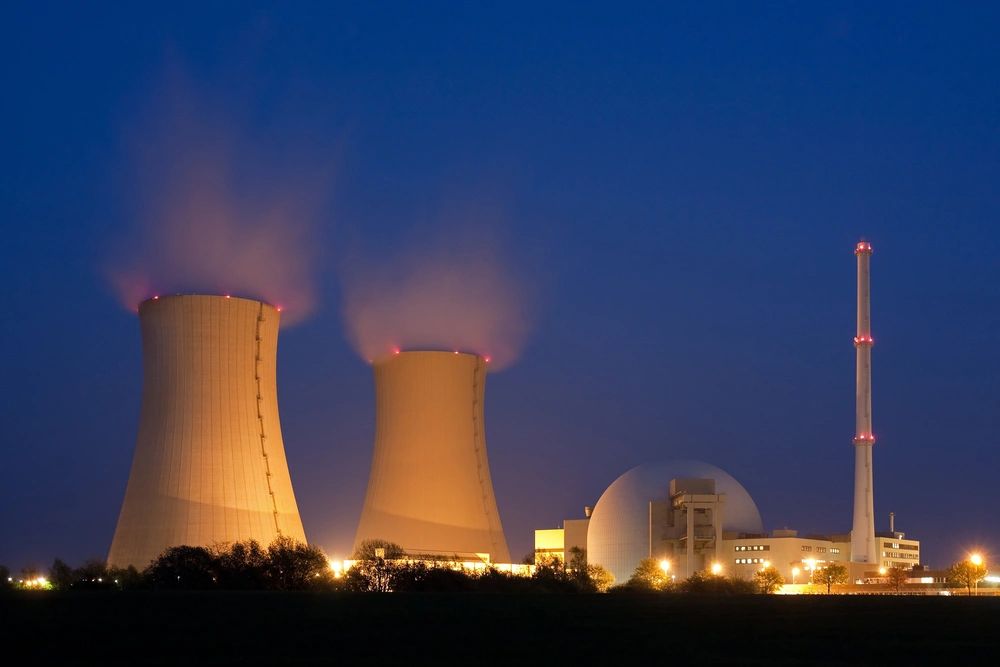 A large nuclear power plant at night with lights on.