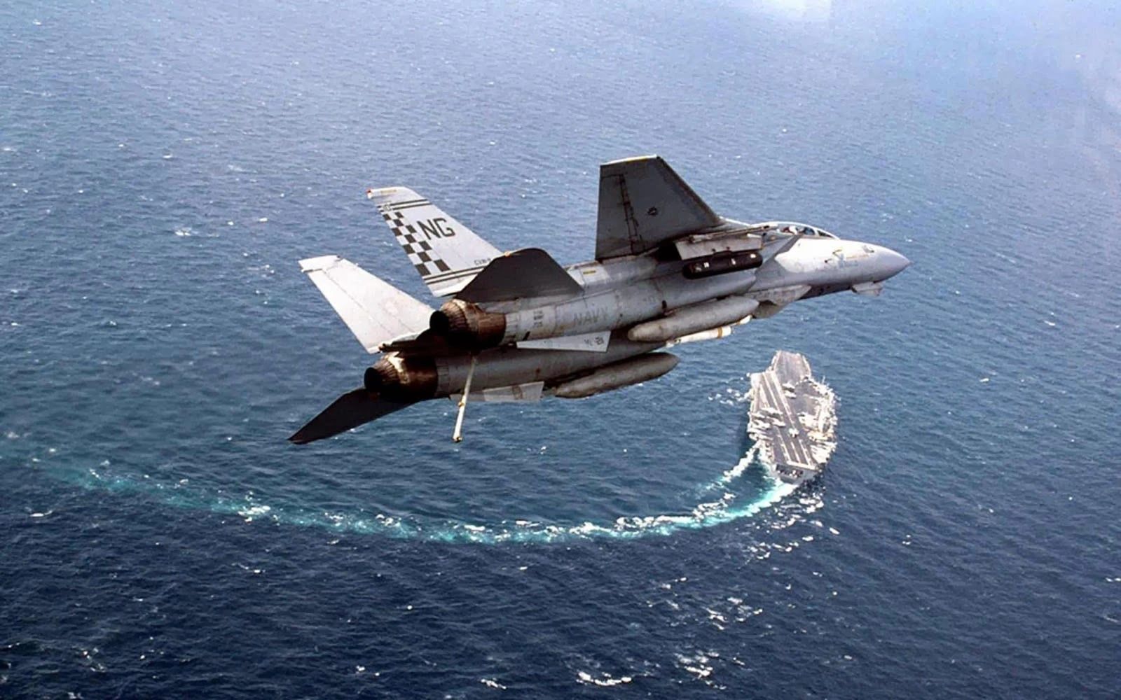 A fighter jet flying over the ocean with a boat in the background.
