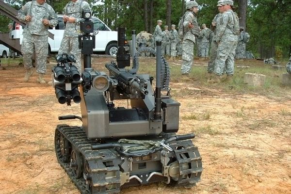 A military robot is parked in the dirt.